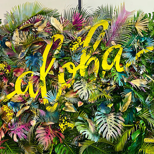 Tropical floral installation made of painted foliage and yellow signage that says Aloha designed by SF.Fleur.