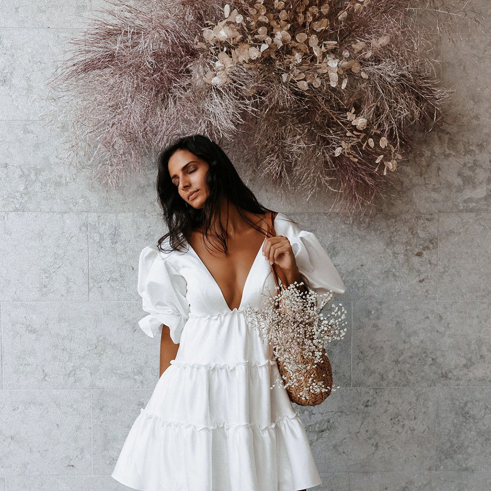 Model wearing a white dress standing in front of a muted blush floral installation designed by SF.Fleur.